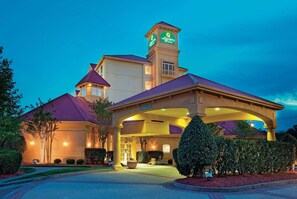 Um hotel com uma torre imponente, entrada coberta e paisagismo bem iluminado.