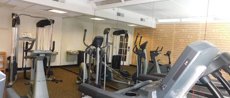 A gym with various exercise machines, a mirrored wall, and a carpeted floor.