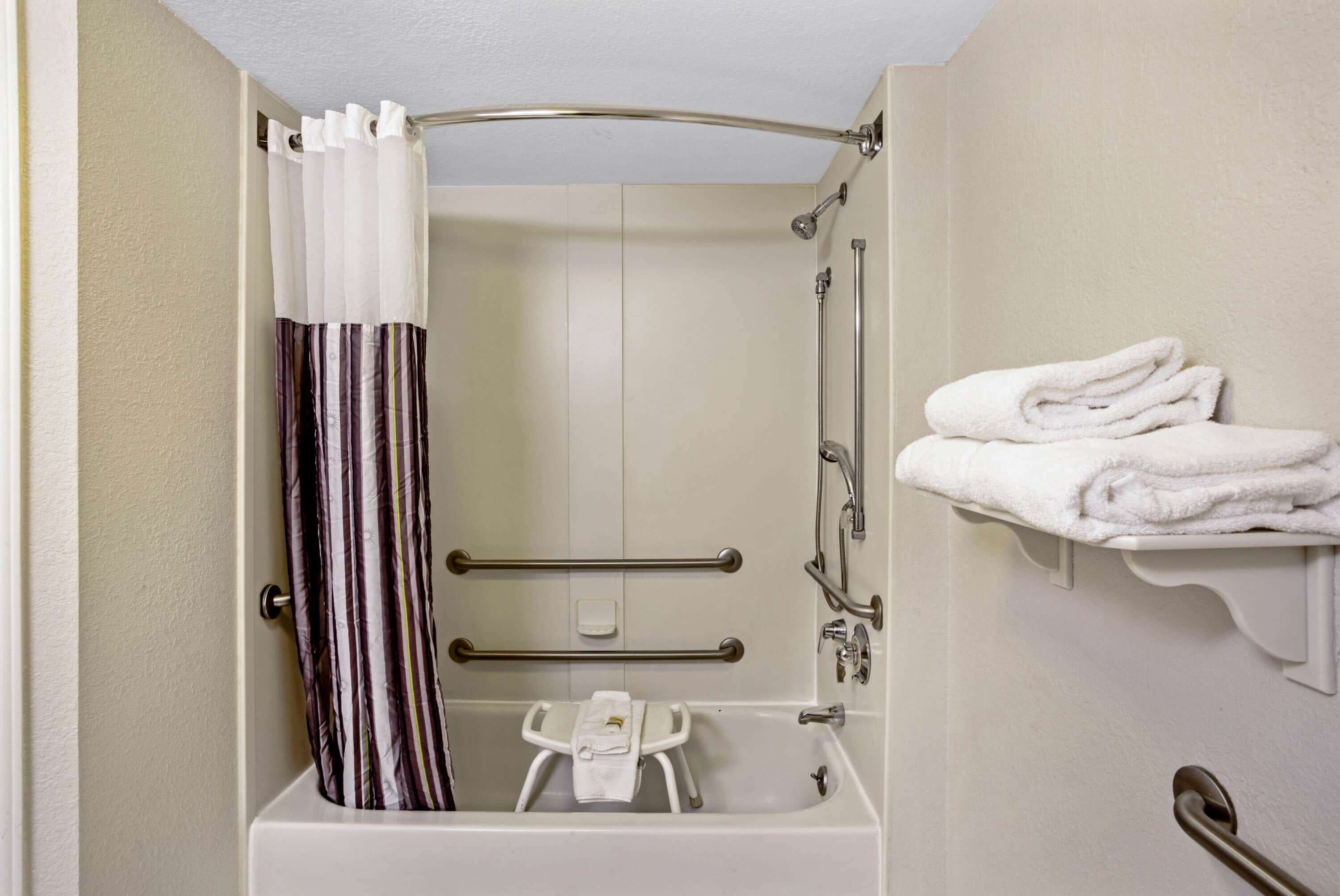 A bathroom with a walk-in shower, grab bars, a white towel rack, and a small white stool.