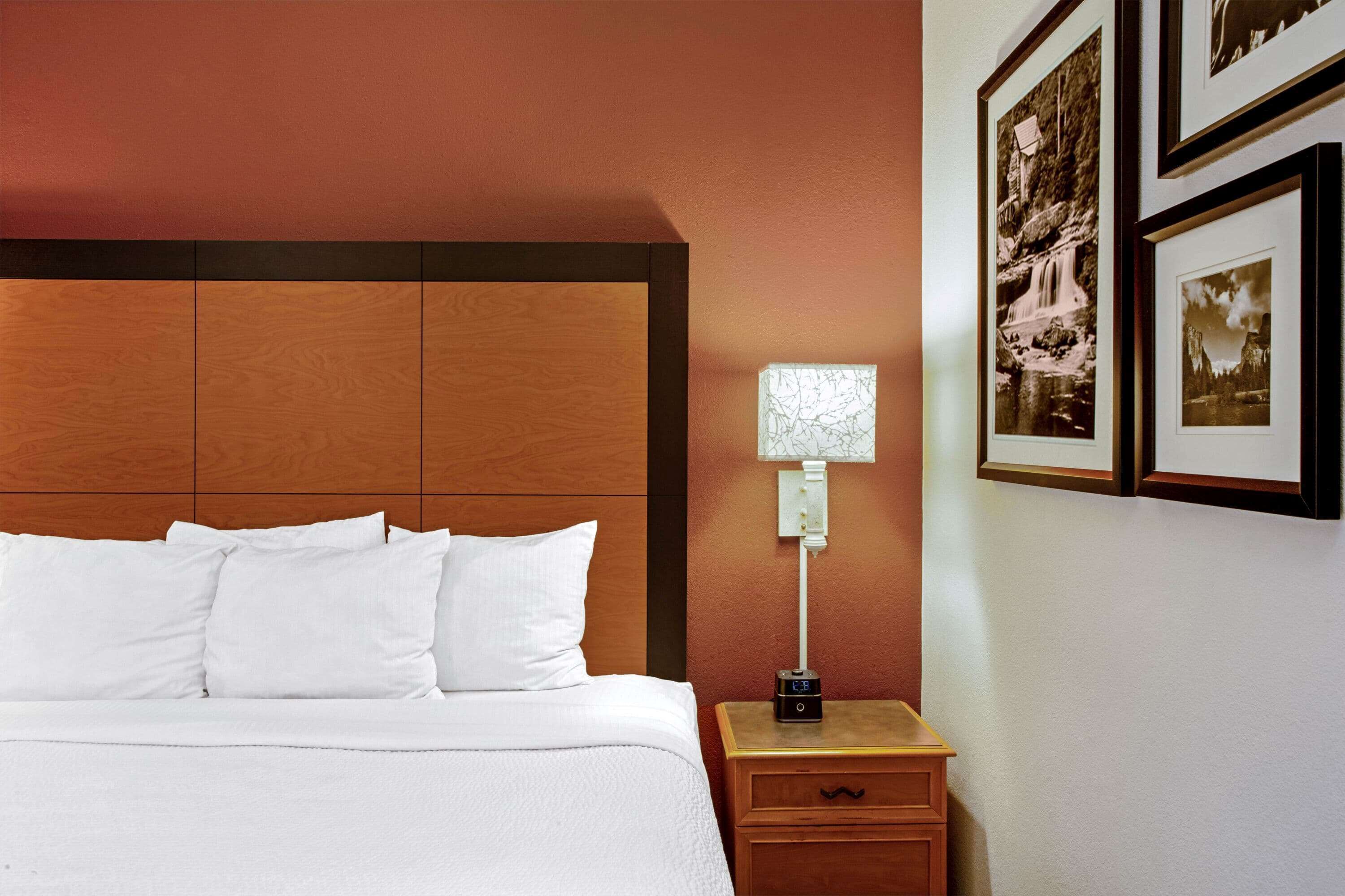 A hotel room with a large bed, a nightstand with a lamp, and framed pictures on the wall.