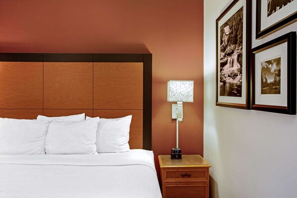A hotel room with a large bed, a nightstand with a lamp, and framed pictures on the wall.