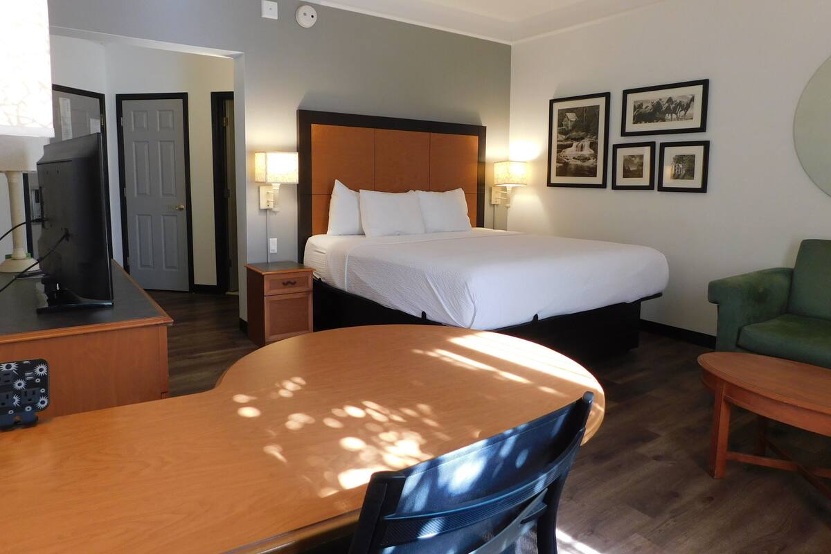A hotel room with a bed, a desk with a computer, a chair, and a table.