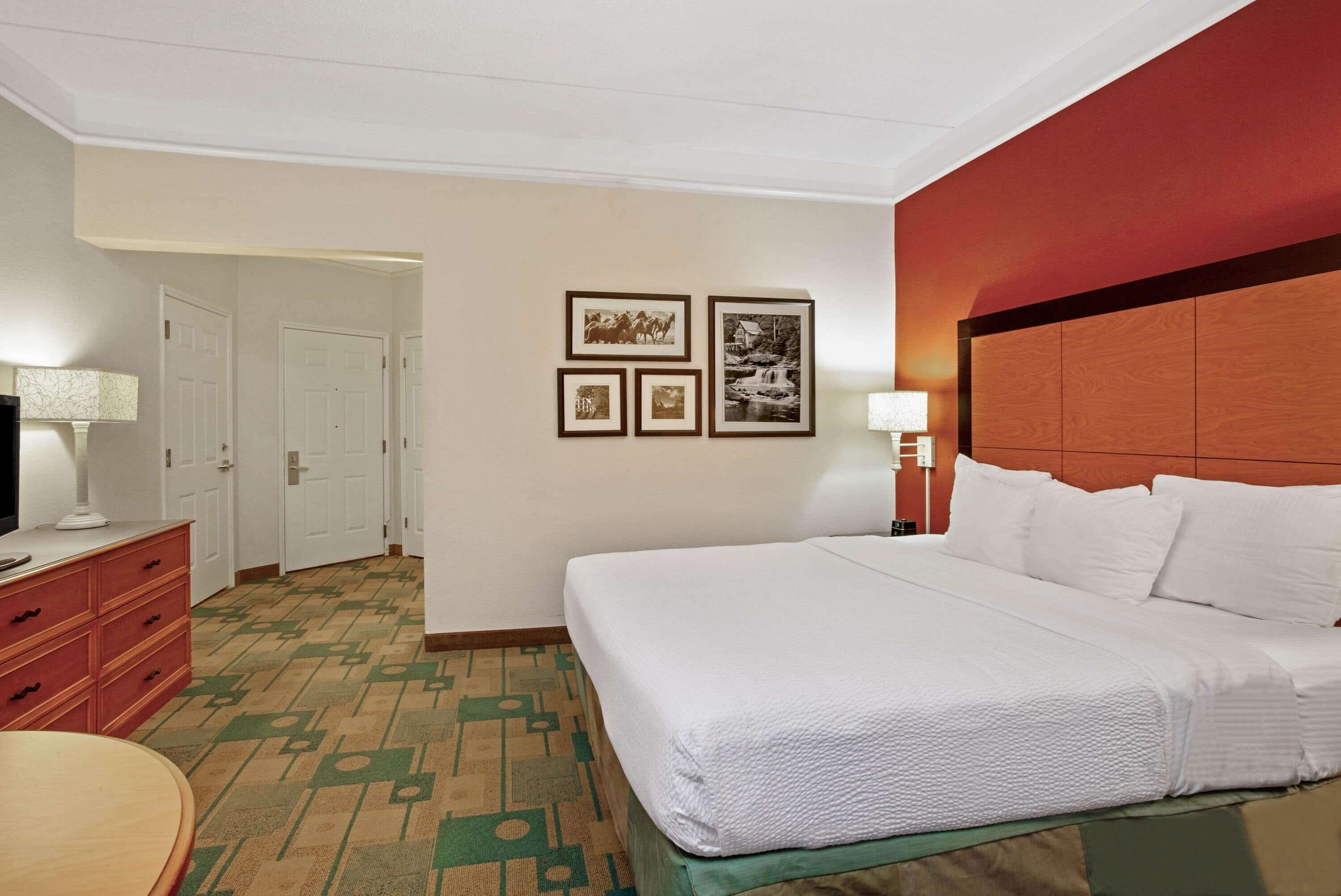 A hotel room with a large bed, a desk with a lamp, a dresser, and a carpeted floor.