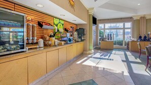 A hotel reception area with a counter displaying food items, a large window with natural light, and a sign reading "La Quinta".