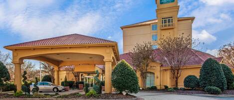 A hotel with a covered entrance, a tower with a sign, and well-maintained landscaping.