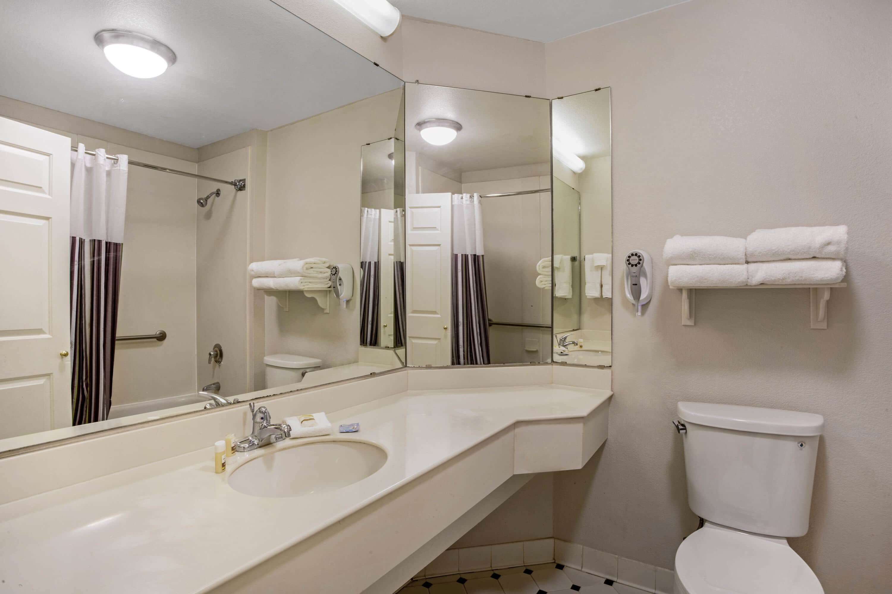 A bathroom with a large mirror, a sink, a toilet, and a towel rack.