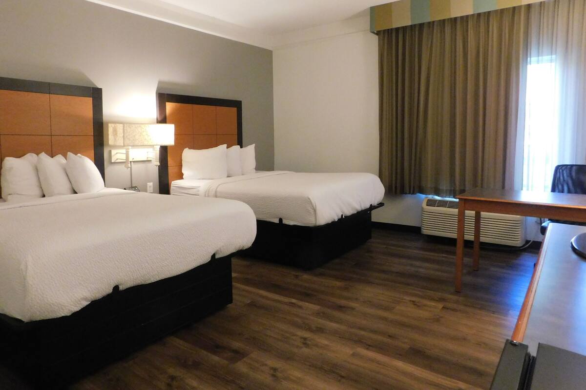 A hotel room with two beds, a desk, a chair, a lamp, and a window with curtains.