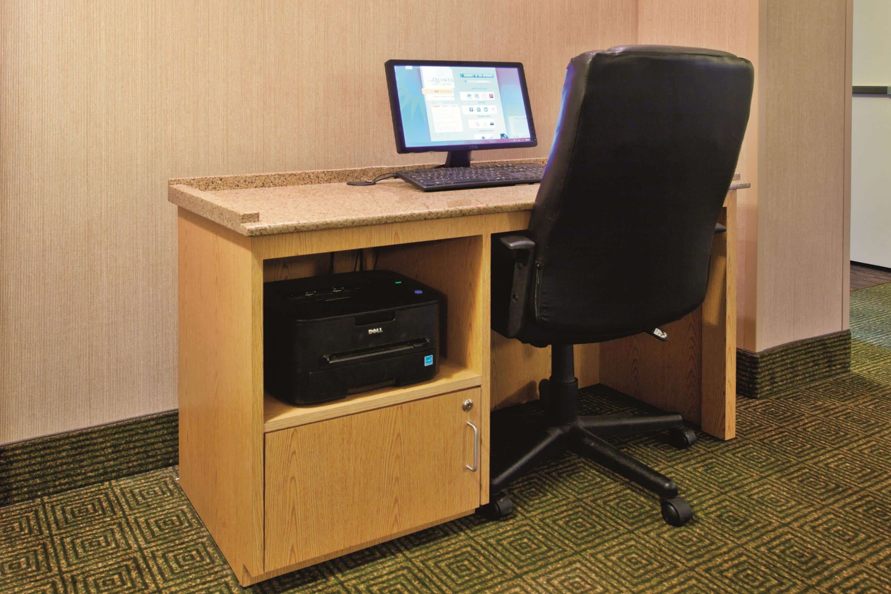 A wooden desk with a computer monitor, keyboard, and printer.