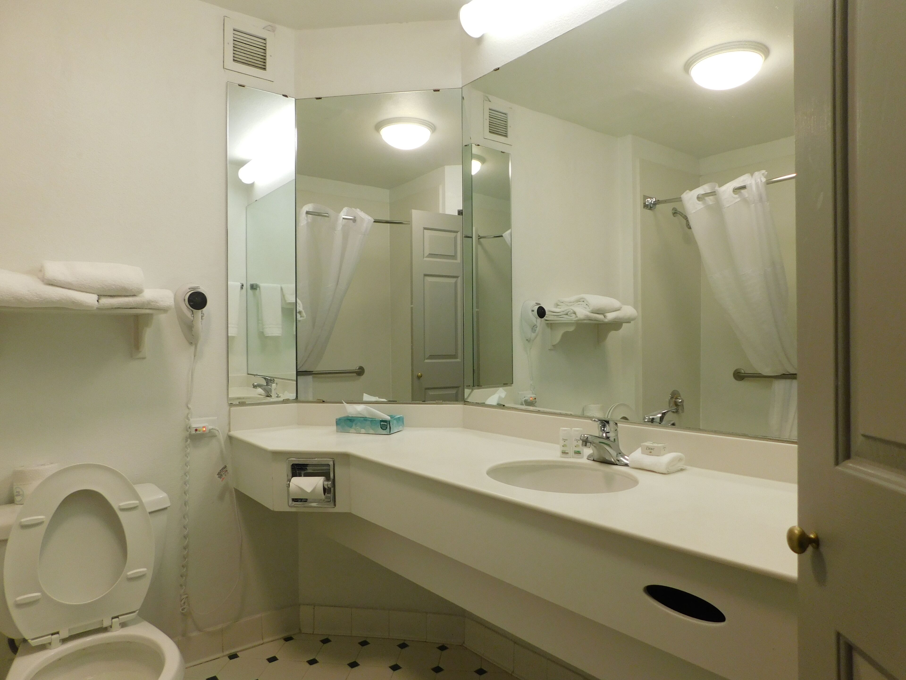 Un baño con inodoro, lavabo y espejos. Hay toallas y un secador de pelo en la pared.