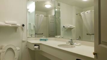 Un baño con inodoro, lavabo y espejos. Hay toallas y un secador de pelo en la pared.