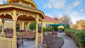 A covered outdoor seating area with chairs and a gazebo, surrounded by landscaped bushes and a pathway.