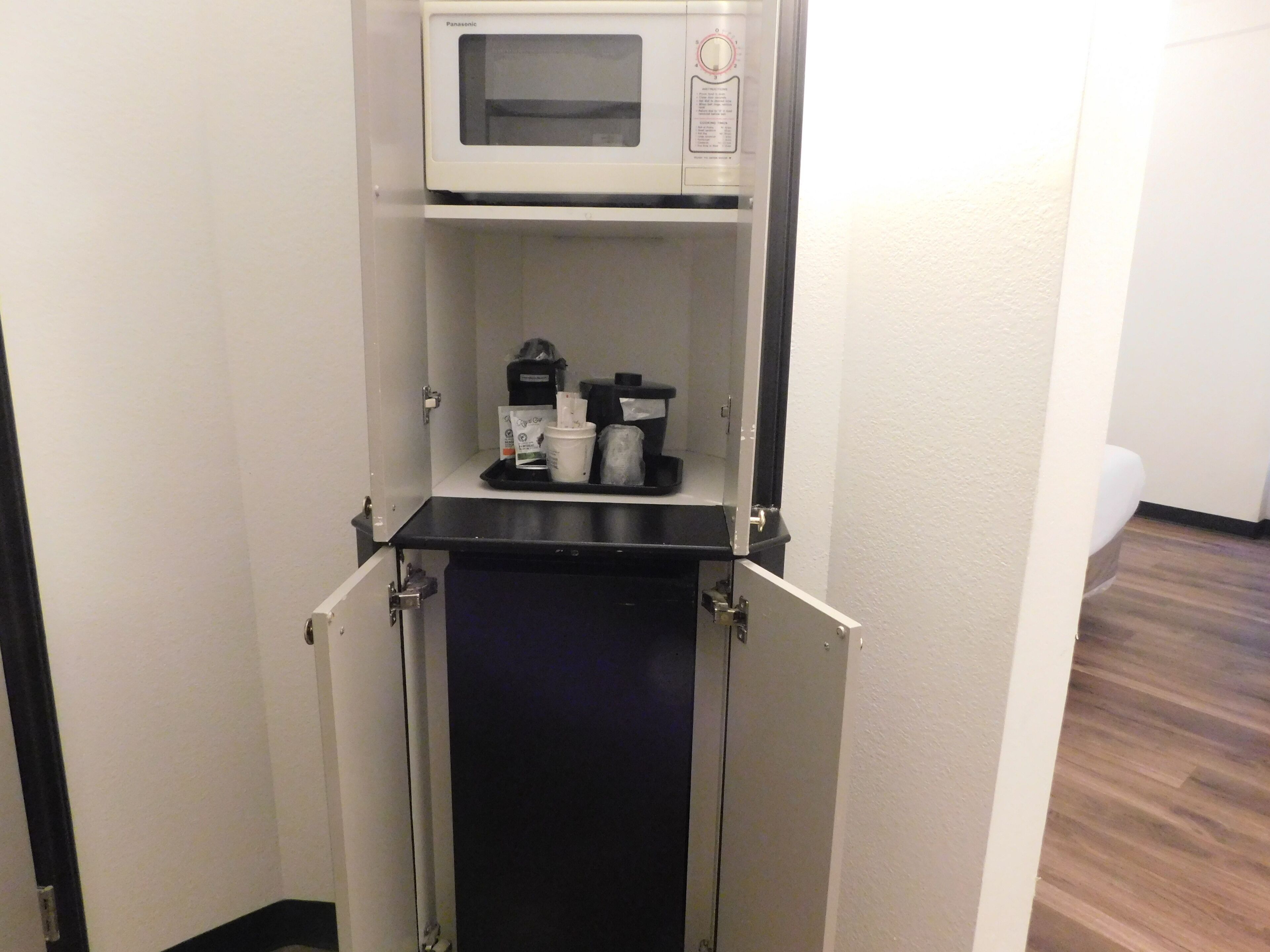 A compact kitchenette with a microwave, coffee maker, and storage shelves.