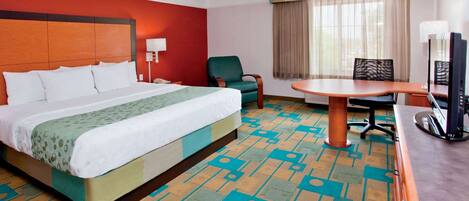 A hotel room with a large bed, a desk with a chair, a television, and a window with curtains.