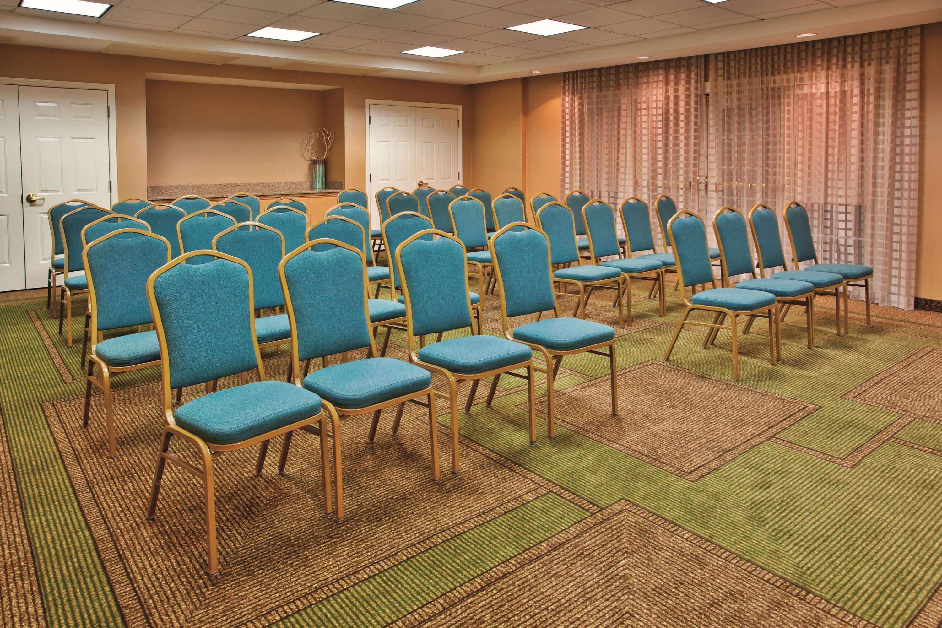 A conference room with rows of blue chairs and a carpeted floor.