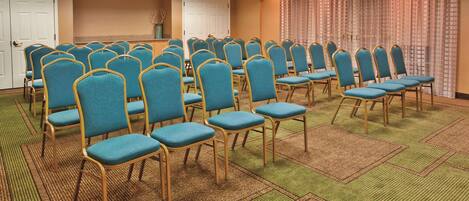 Un salón de conferencias con filas de sillas azules y piso alfombrado.