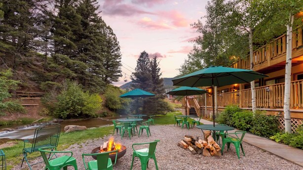 An outdoor seating area with green chairs and tables, a fire pit, and a view of a river and forest. - Best Western Rivers Edge (Red River)