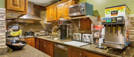 A kitchen with wooden cabinets, granite countertops, a microwave, a coffee maker, and a refrigerator.