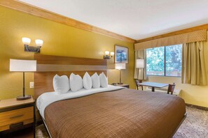 A hotel room with a large bed, two bedside tables, a desk, and a window with curtains.