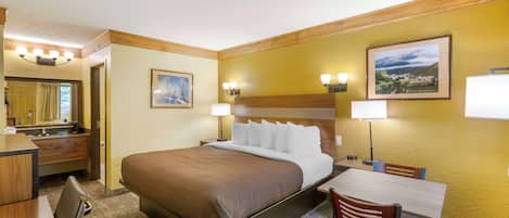 Habitación de hotel con cama, escritorio, silla y baño con espejo y lavamanos.