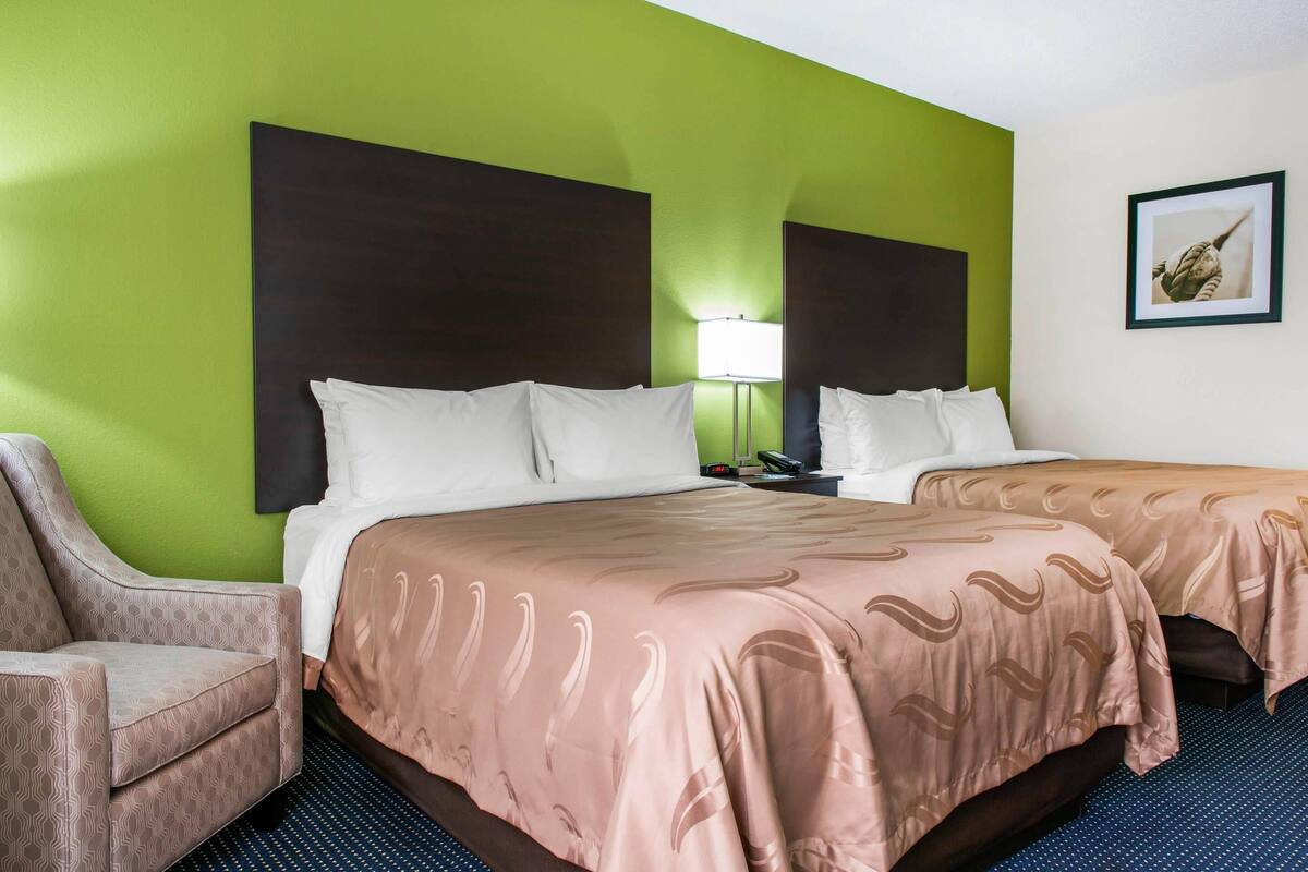 Une chambre d’hôtel avec deux lits, une chaise, une lampe et un tableau encadré au mur.