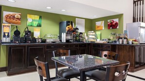 A breakfast bar with waffle and coffee machines, a refrigerator, and a dining area with a table and chairs.