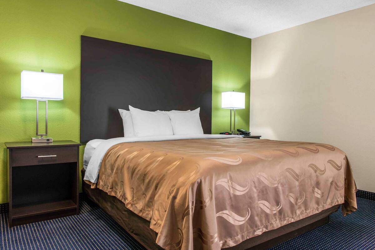 Une chambre d’hôtel avec un lit, deux tables de chevet et deux lampes fixées au mur.