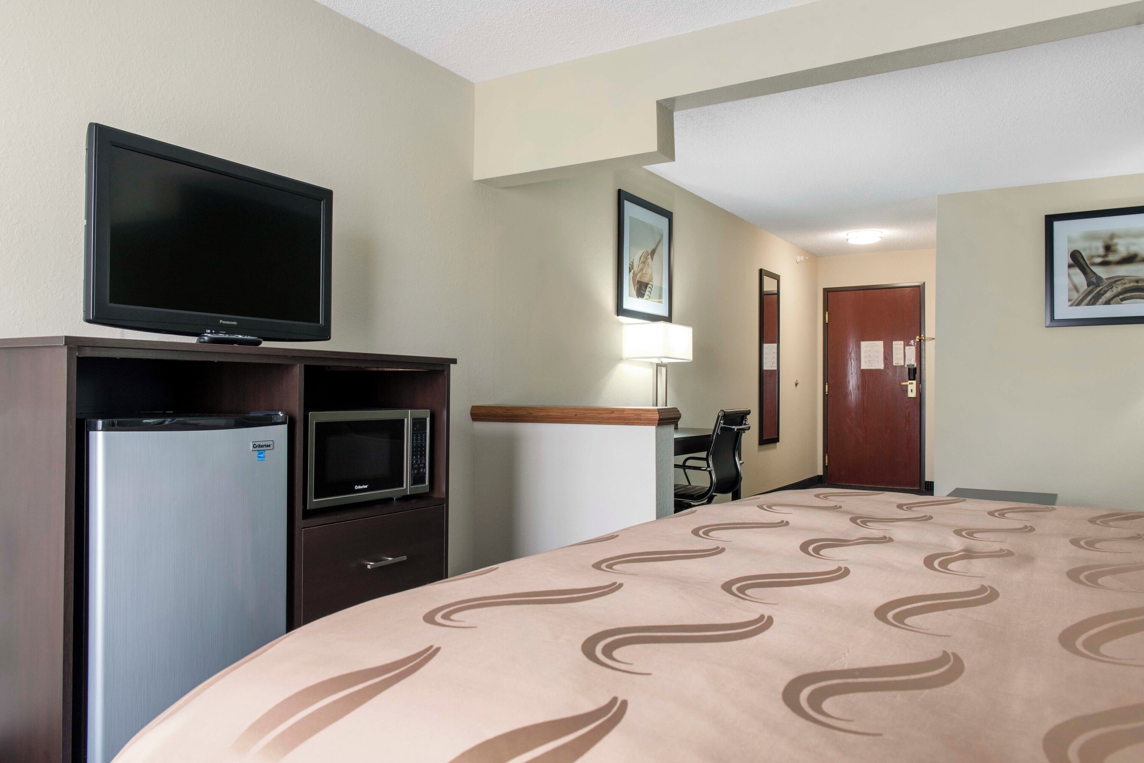 A hotel room with a bed, a television, a refrigerator, a microwave, a desk, and a chair.