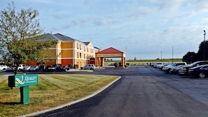 A hotel with a red-roofed entrance, a parking lot with several cars, and a sign for Quality Inn & Suites.