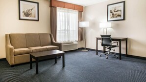 Une chambre d’hôtel avec un canapé, un bureau, une chaise, une lampe et deux tableaux encadrés accrochés aux murs.