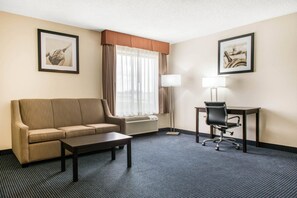 Ein Hotelzimmer mit Sofa, Schreibtisch, Stuhl, Lampe und zwei gerahmten Bildern an den Wänden.