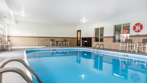A swimming pool with clear water, a lifebuoy on the wall, and a door leading to another room.