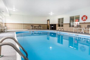 A swimming pool with clear water, a lifebuoy on the wall, and a door leading to another room.