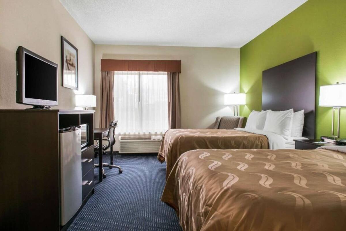 A hotel room with two beds, a desk, a television, and a window with curtains.