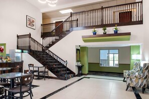 Un vestíbulo amplio con una escalera, una zona de comedor con sillas y una mesa, y un mostrador de recepción.
