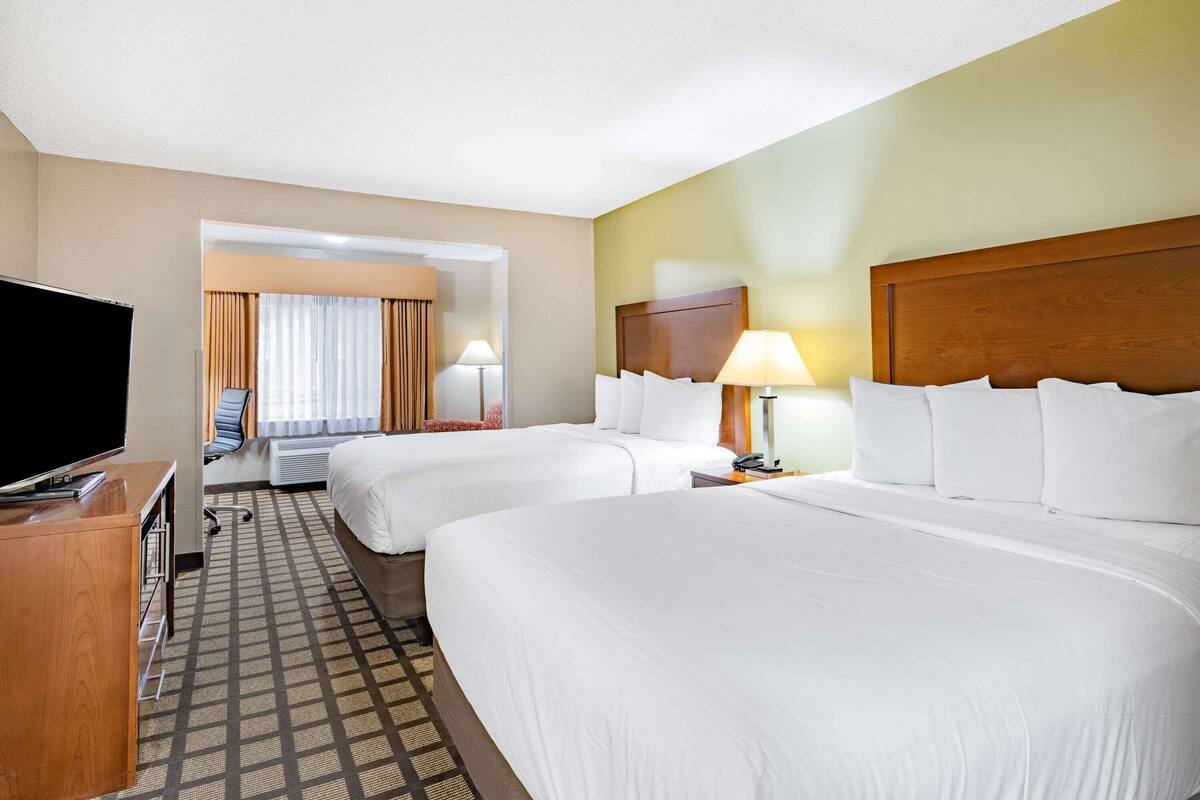 A hotel room with two beds, a TV, a desk, and a chair.