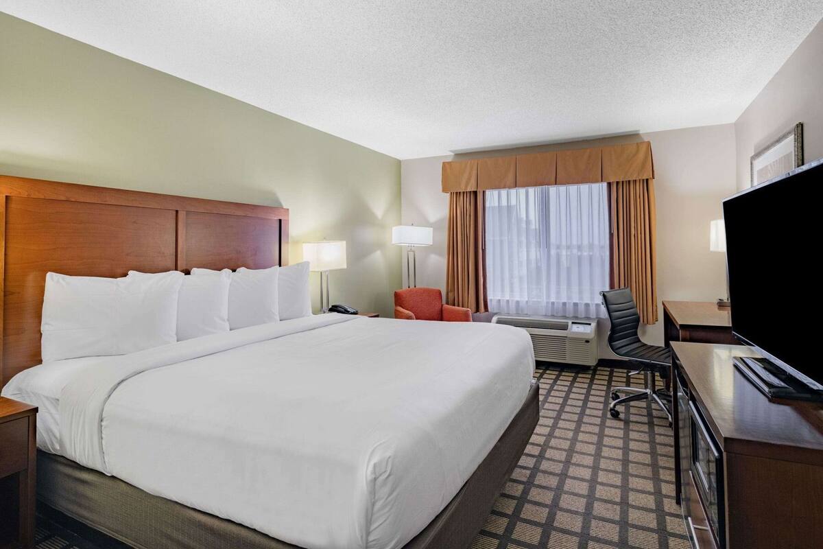 A hotel room with a large bed, a desk, a chair, a television, and a window with curtains.