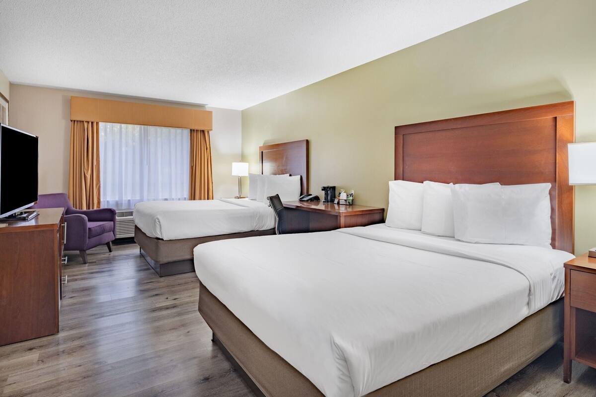 A hotel room with two beds, a desk, a chair, a TV, and a window with curtains.