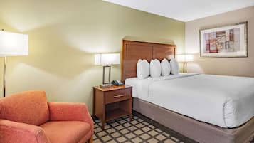A hotel room with a bed, a nightstand with a lamp, a chair, and a patterned floor.