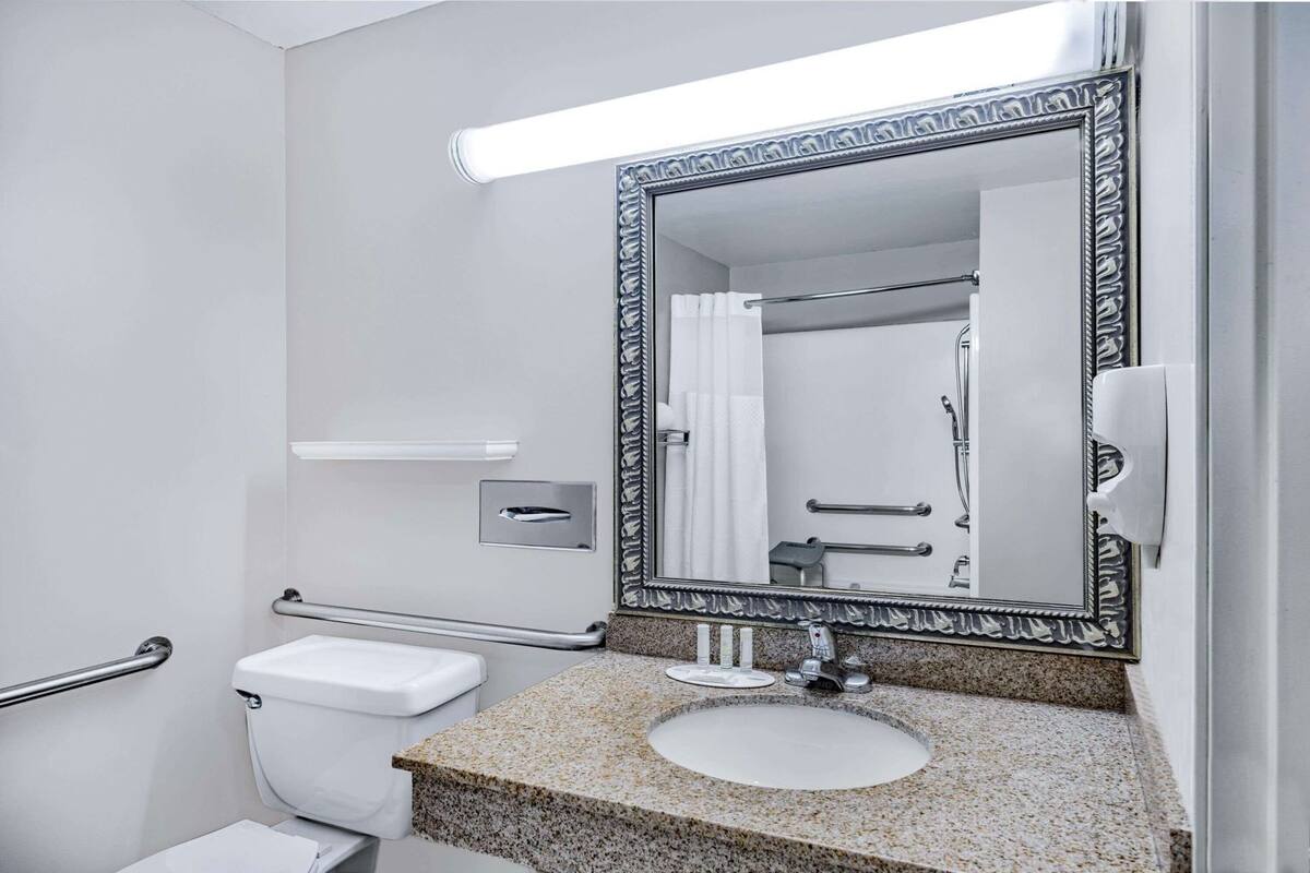 A bathroom with a toilet, sink, mirror, and shower.