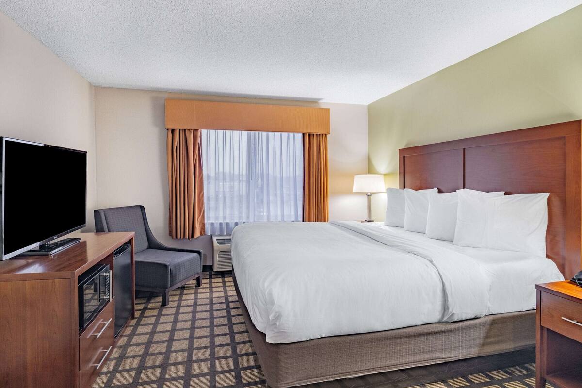 A hotel room with a large bed, a desk with a TV, a chair, and a window with curtains.