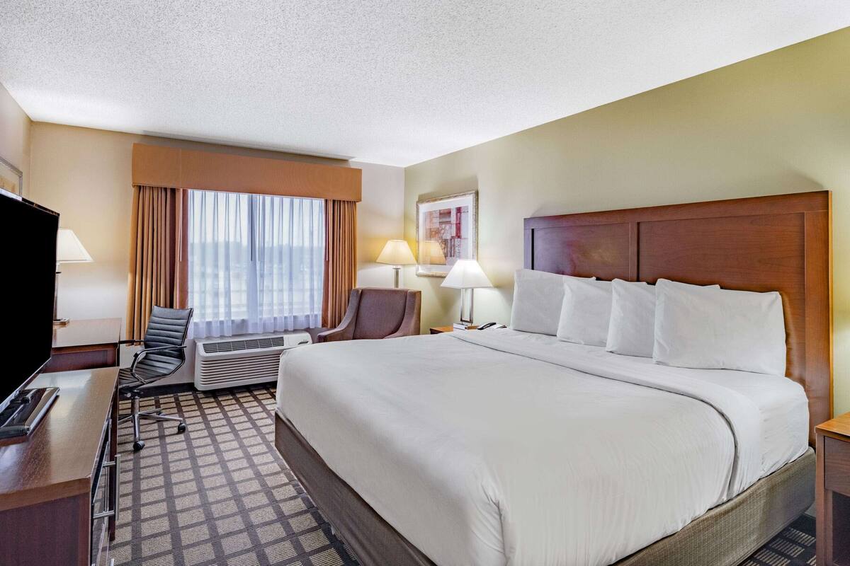A hotel room with a large bed, a desk with a chair, a television, and a window with curtains.