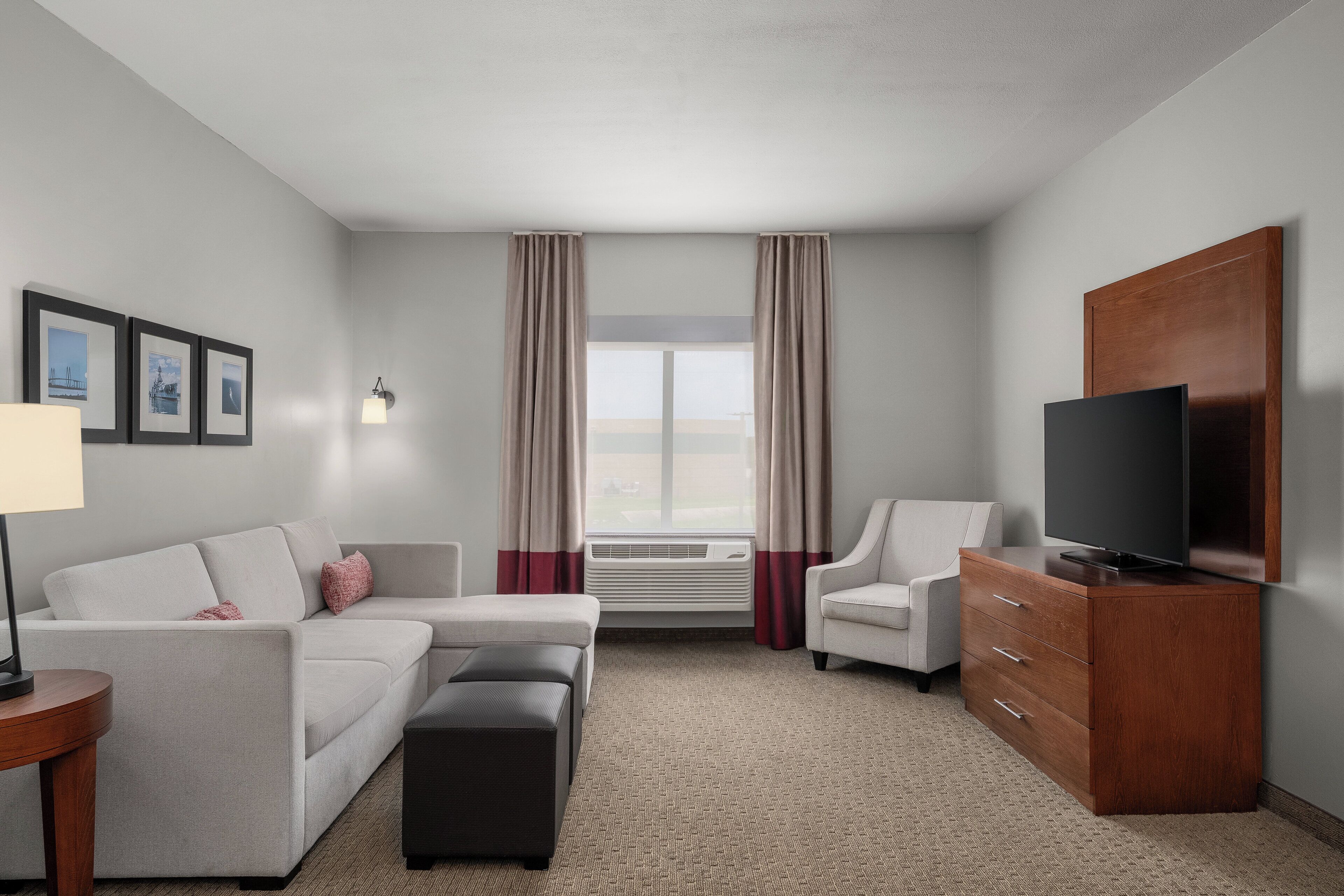 Une chambre d’hôtel équipée d’un canapé, d’un fauteuil, d’un pouf, d’une télévision et d’une armoire en bois.
