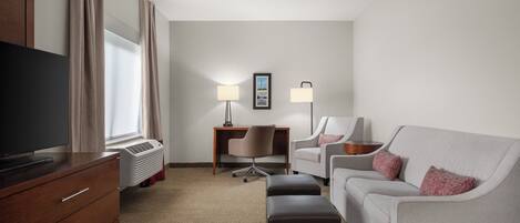 A hotel room with a flat-screen TV, a desk, two chairs, a sofa, and a standing lamp.