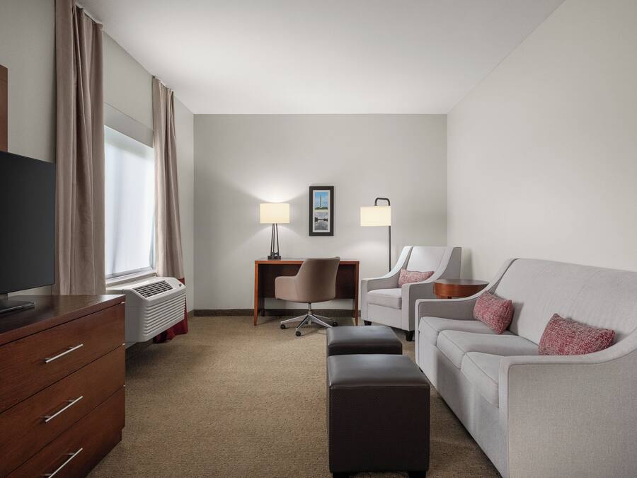 Ein Hotelzimmer mit Flachbildfernseher, Schreibtisch, zwei Stühlen, einer Couch und einer Stehlampe.