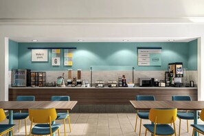 Een modern café met een balie, een zitgedeelte en diverse stations voor eten en drinken.