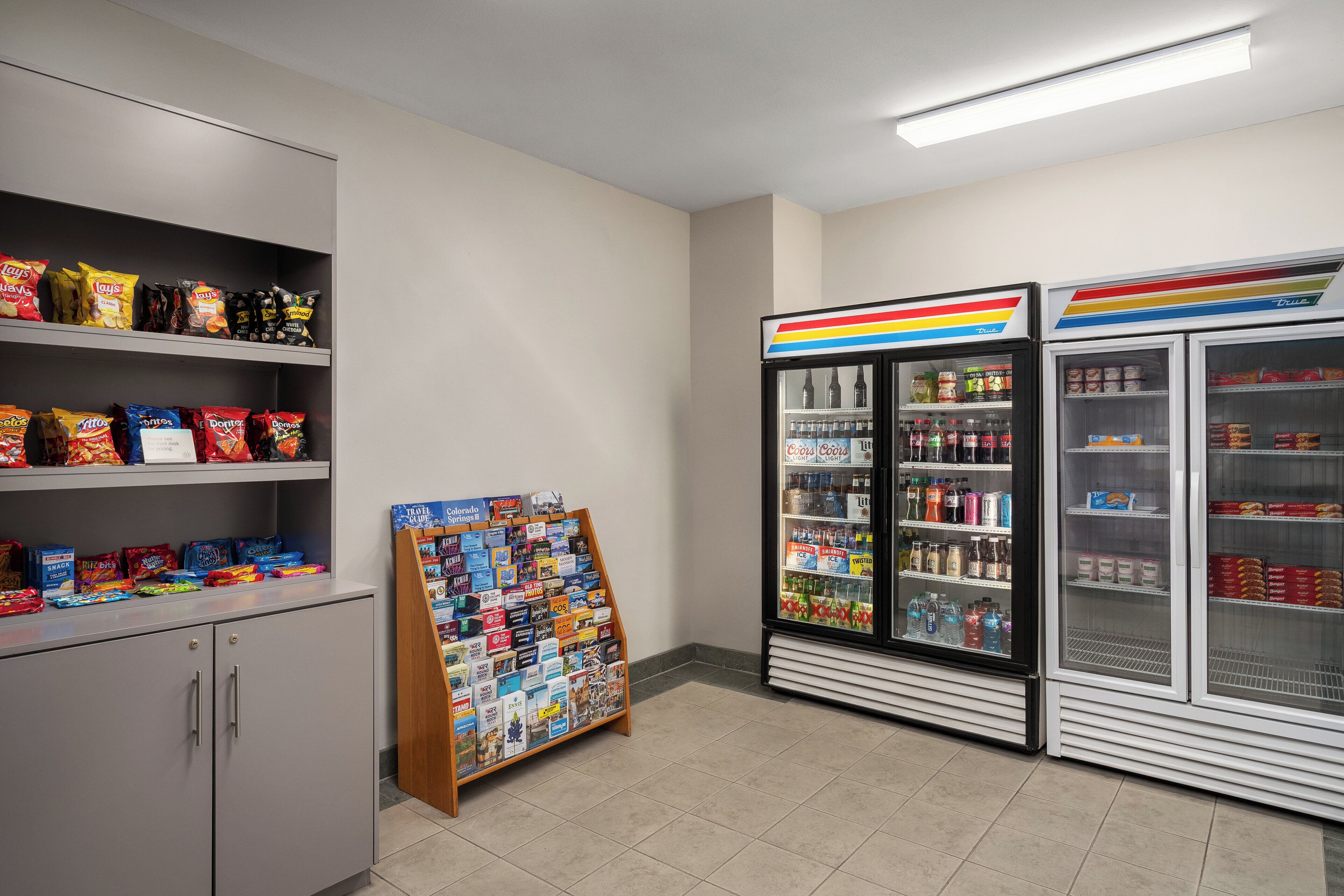 A snack and beverage section with shelves of chips, a display of travel books, and refrigerated cases with drinks.