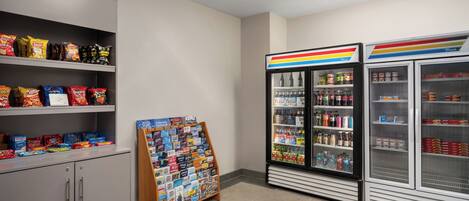 A snack and beverage section with shelves of chips, a display of travel books, and refrigerated cases with drinks.