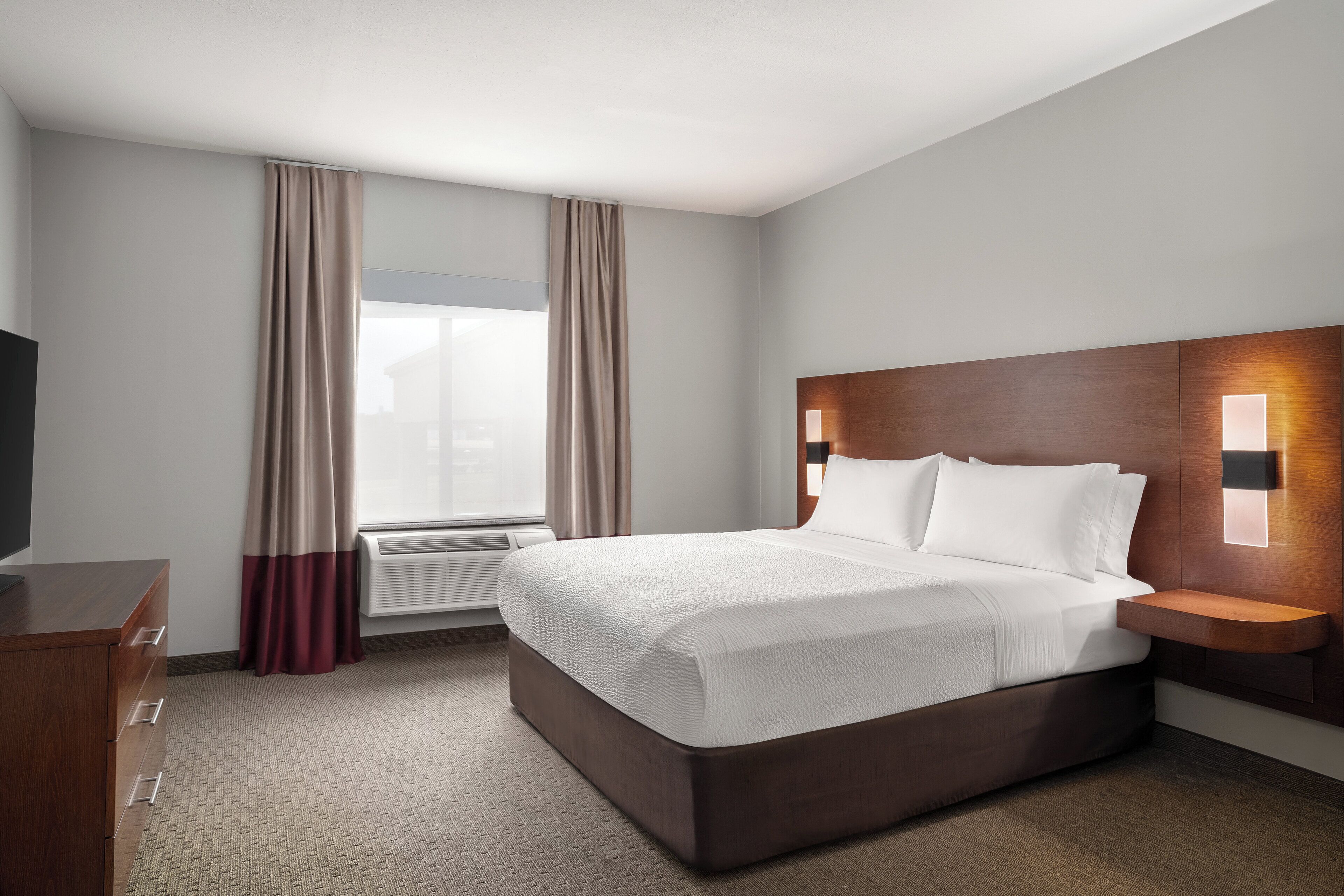 A hotel room with a bed, a desk, a chair, a TV, and a window with curtains.
