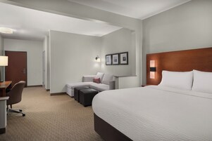 A hotel room with a large bed, a desk with a chair, a sofa, and a small table.