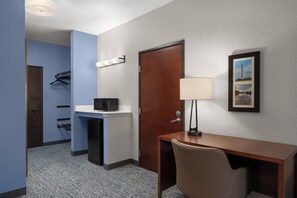 A hotel room with a desk, chair, microwave, and a door with a coat rack.